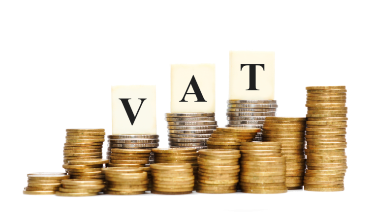 Blocks displaying the letters 'V,' 'A,' and 'T,' standing for Value Added Tax, are placed on stacks of coins against a bright white background. This visually represents the concept of a VAT increase, aligning with discussions on Indonesia's VAT hike in 2025.