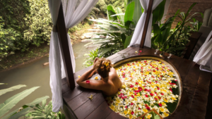 A serene outdoor wellness retreat in Bali, Indonesia, featuring a luxurious flower bath overlooking a lush tropical river. This setting exemplifies wellness tourism in Indonesia, offering relaxation, rejuvenation, and holistic well-being amidst nature.