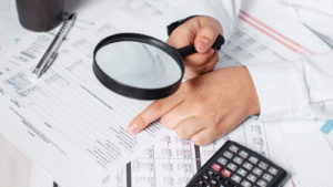 Businessman using a magnifying glass to review an annual balance sheet. Illustrating the concept of internal audit, auditing tax, and analyzing return on investment.