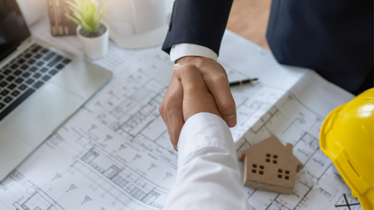 Two business professionals shaking hands over architectural blueprints, Illustrating an Investor in Bali Investing in a property, with a laptop, hard hat, and model house.