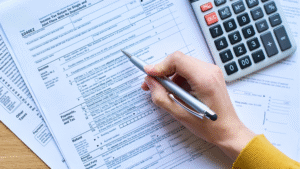 A person filling out tax forms with a calculator beside them, representing the documentation required for tax clearance in Indonesia during company closure.