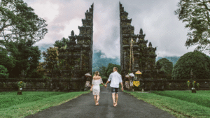 Australian couple walks hand-in-hand towards a traditional Balinese temple gate symbolizing the need for Bali visa for Australians.