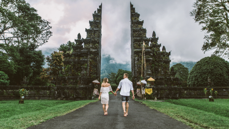 Australian couple walks hand-in-hand towards a traditional Balinese temple gate symbolizing the need for Bali visa for Australians.