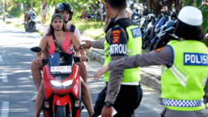 Foreign tourists on a motorbike are stopped by Balinese police officers enforcing Bali rules on traffic and legal driving requirements.