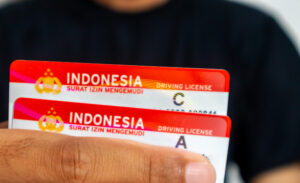 A man in black clothes holding a driving license, signifying driving license renewal in Indonesia.