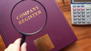 A magnifying glass held over a maroon company register book with gold lettering, symbolizing company incorporation in Indonesia.