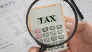 Close-up of a calculator displaying the word TAX under a magnifying glass, symbolizing taxation in Indonesia and financial compliance.