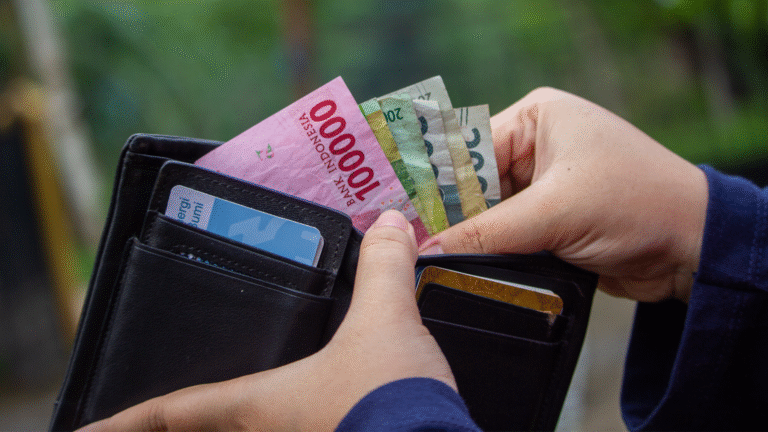 A person holding Indonesian rupiah banknotes from a wallet, representing payment and budgeting for the Bali tourist tax.