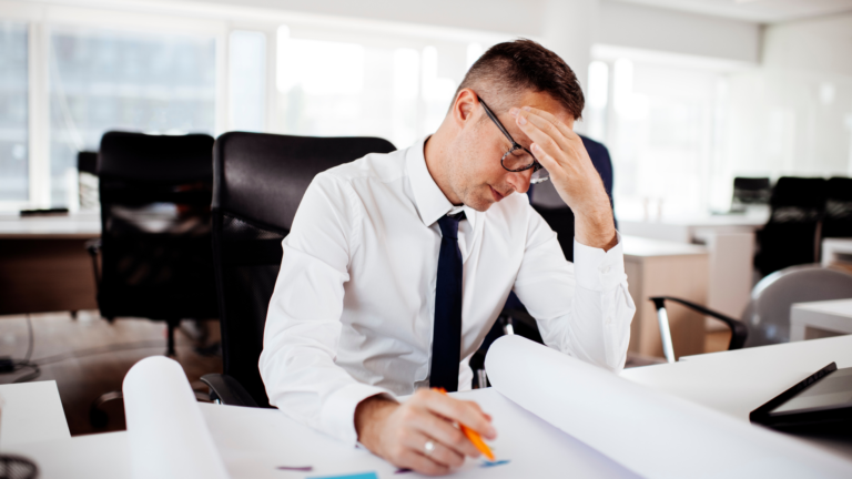 A stressed businessman sitting at his desk reviewing documents, illustrating the challenges many entrepreneurs face when starting a business in Bali.