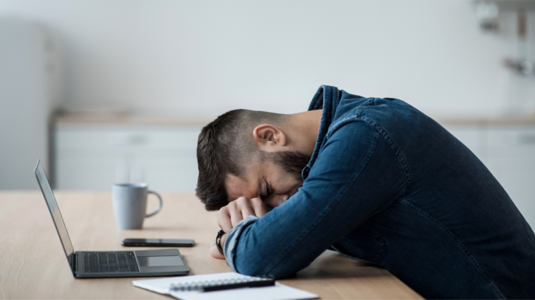 Exhausted businessman sleeping at his desk beside a laptop, symbolizing stress and costly PT PMA legal mistakes during company setup in Indonesia.