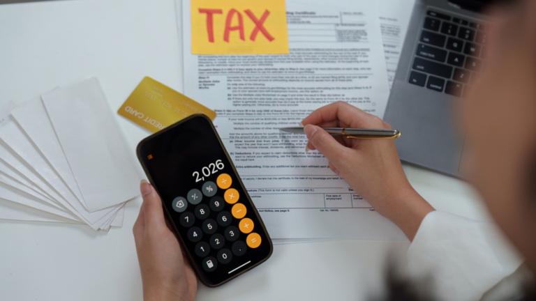 Business professional calculating corporate tax obligations in Indonesia using a smartphone calculator, tax documents, a credit card, and a laptop on an office desk.